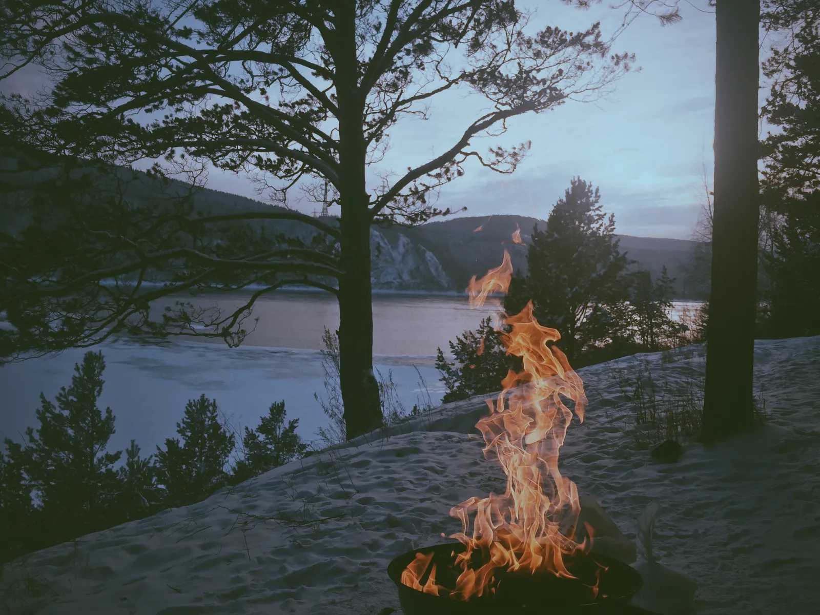 A fire burning on the rocks beside a lake at dusk