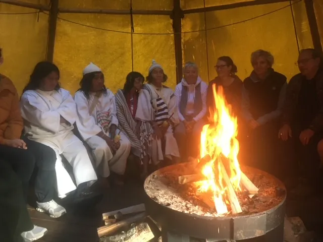 People seated around a fire inside a tent