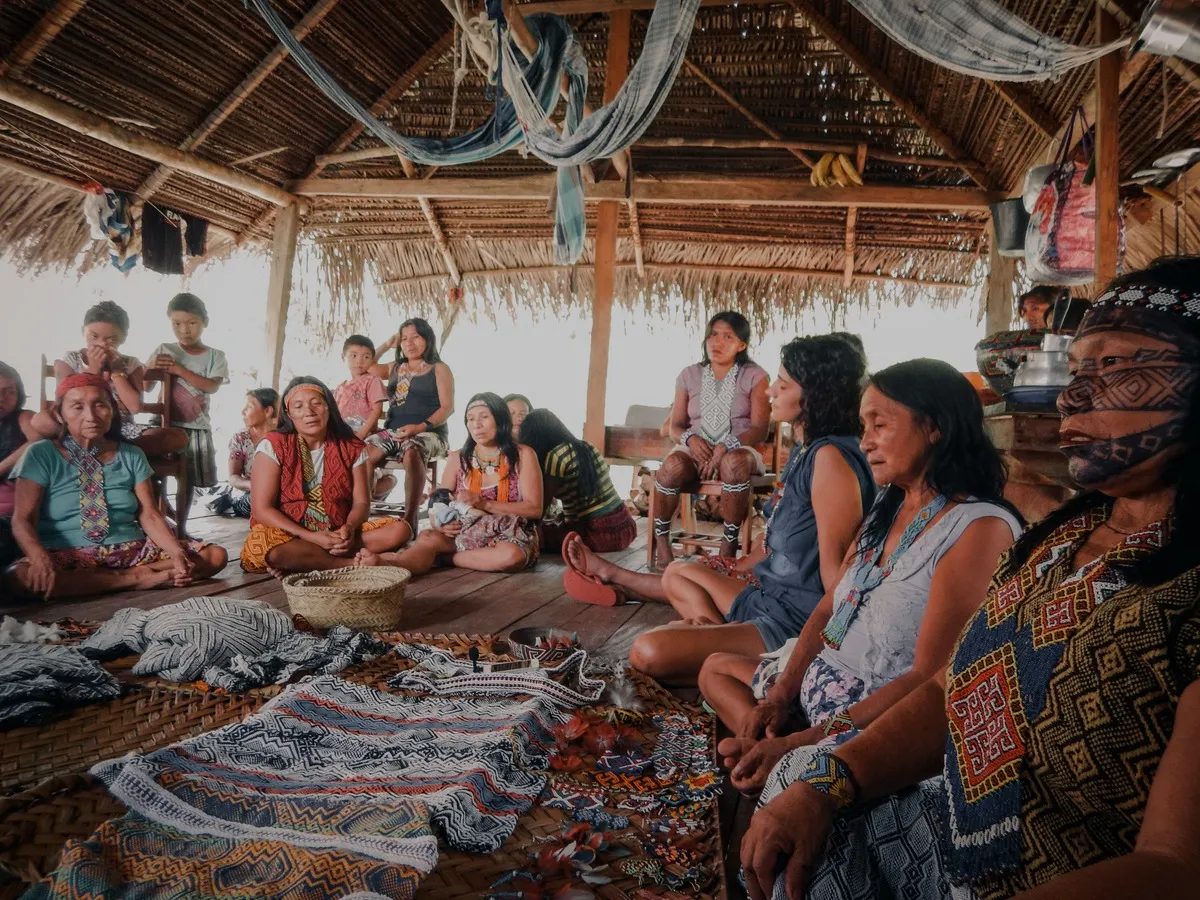 Women seated together in a circle in a thatched hall